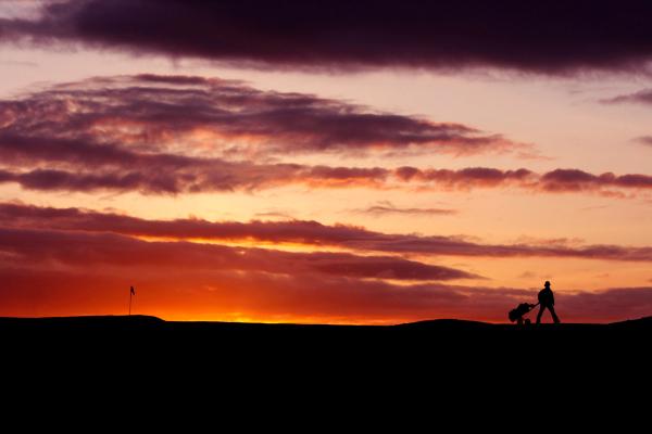 Hombre arrastrando su carro de golf al atardecer