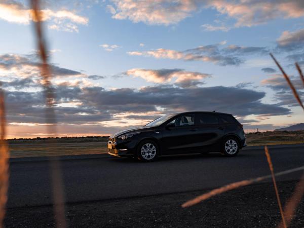 A black car parked on a road at sunset, with blurry tall grass in the foreground.
