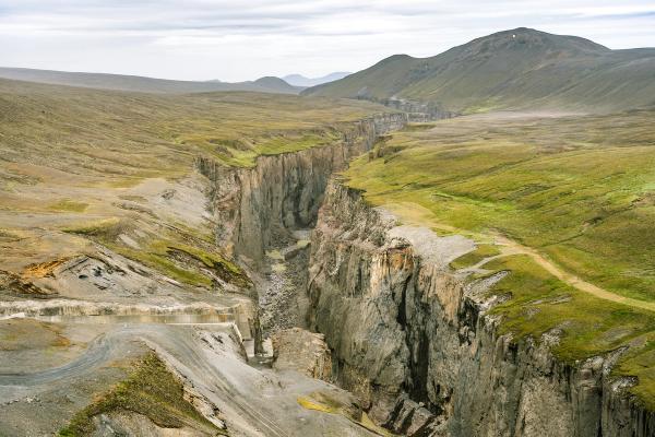 Un profundo cañón atraviesa un vasto paisaje montañoso, verde y marrón, surcado por caminos de tierra.
