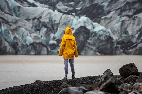 girl in a yellow raincoat admires the powerful big Katla glacier, Iceland