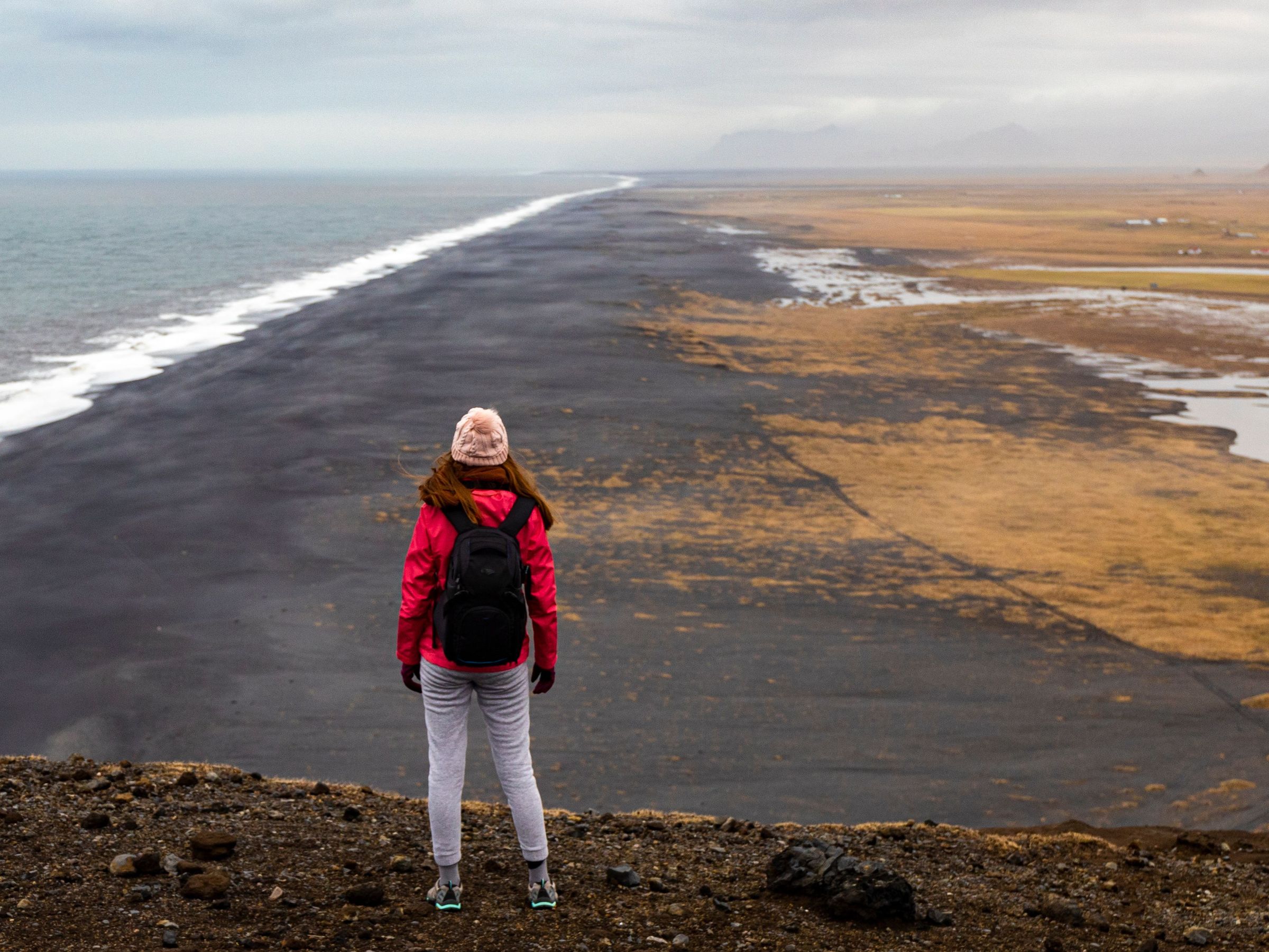 Girl standing on a cliff overlooking a black sand beach in Dyrholaey, Iceland
