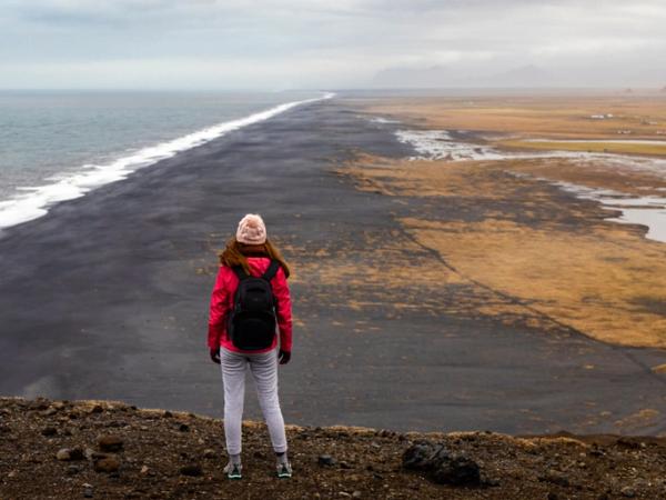 Girl standing on a cliff overlooking a black sand beach in Dyrholaey, Iceland
