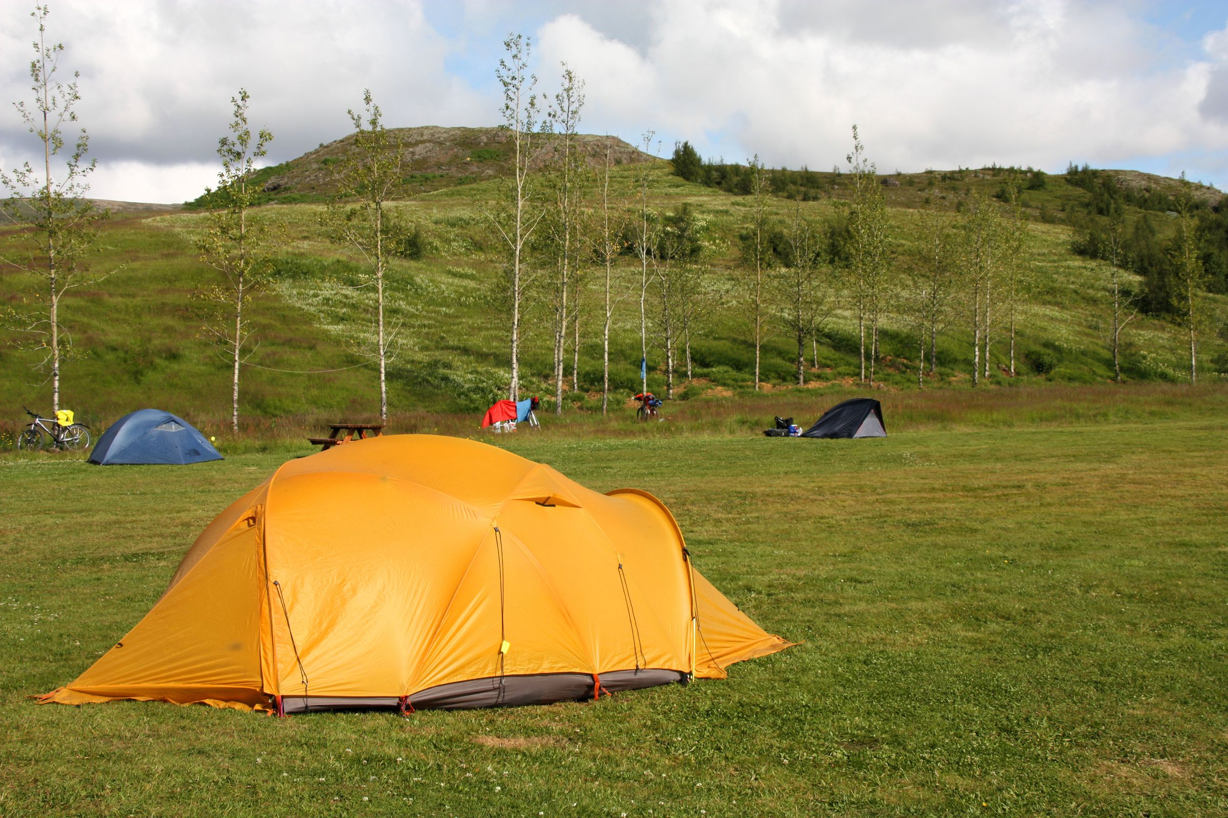 a yellow tent in a grass field with more tents on the background