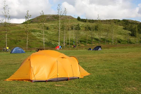una pradera con una tienda de campaña amarilla en primer plano