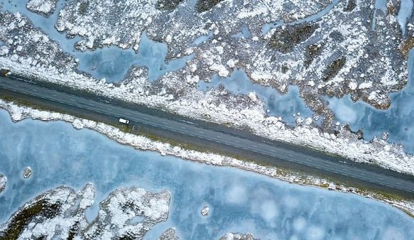 Overhead view of a white car on a road cutting through a snowy, icy landscape.