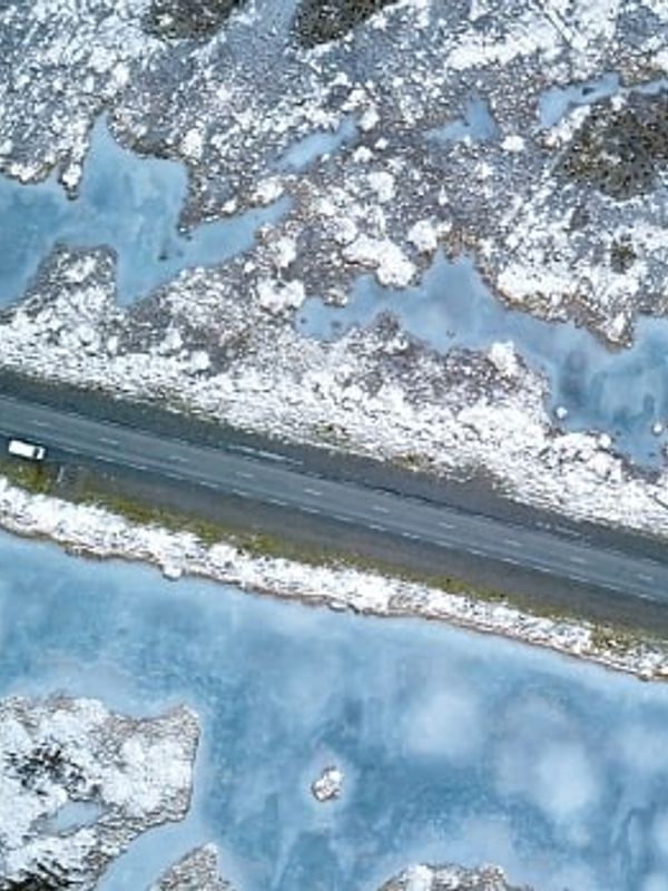 Overhead view of a white car on a road cutting through a snowy, icy landscape.