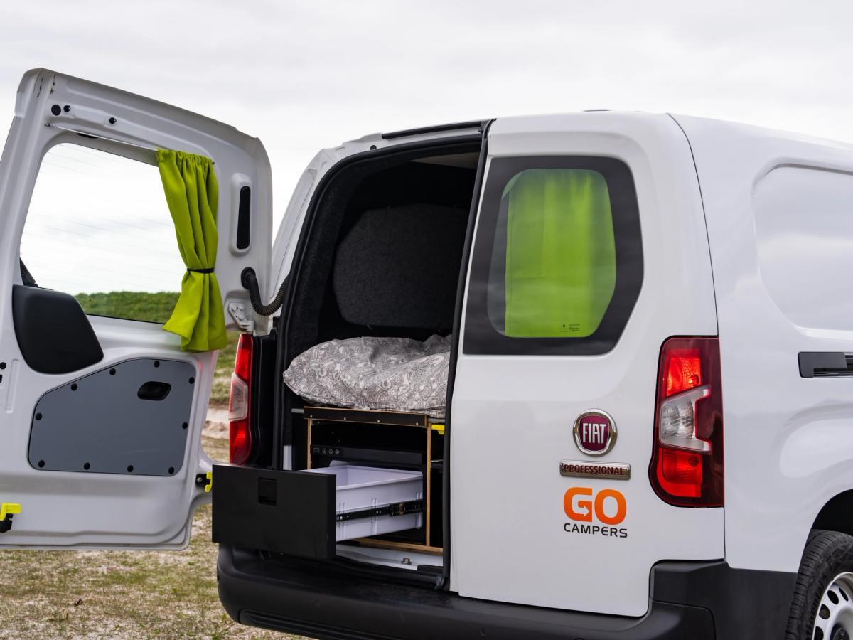 Parte trasera abierta de una autocaravana compacta Parte trasera de una autocaravana compacta con una puerta abierta y el cajón frigorífico extraído debajo de la cama