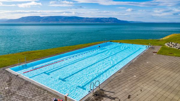 a large swimming pool with a view of the ocean and mountains in the background at Hofsós pool in north iceland.