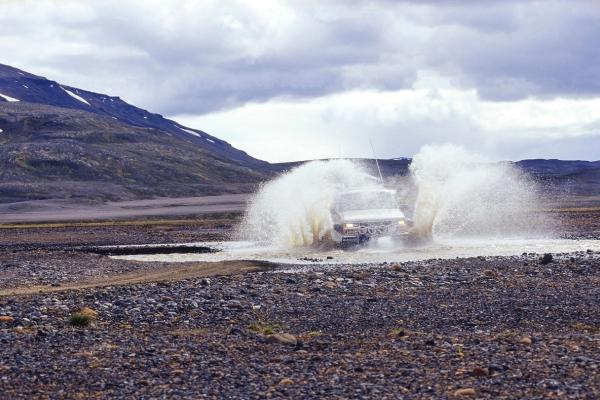 a car is driving through a puddle of water on a dirt road .