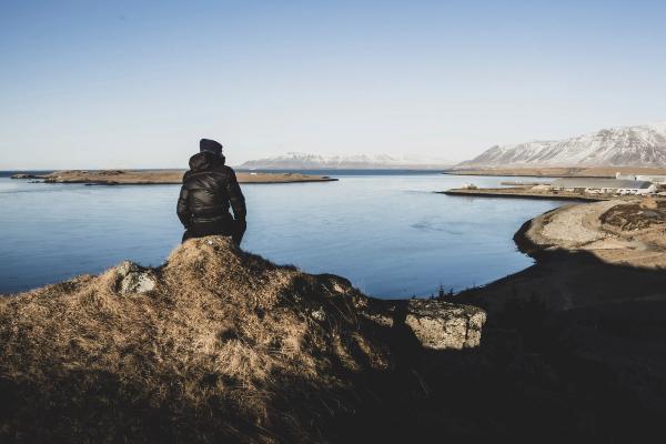 a person is sitting on top of a rock overlooking a body of water .