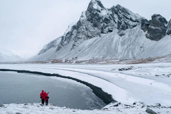 two people are standing on the shore of a snow covered lake .
