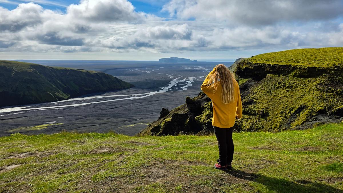 a woman in a yellow sweater is standing on top of a hill overlooking a river .