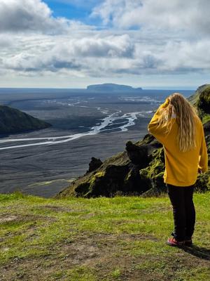 a woman in a yellow sweater is standing on top of a hill overlooking a river .