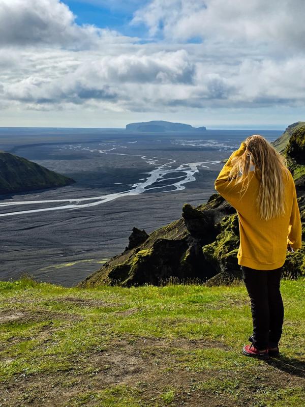 a woman in a yellow sweater is standing on top of a hill overlooking a river .