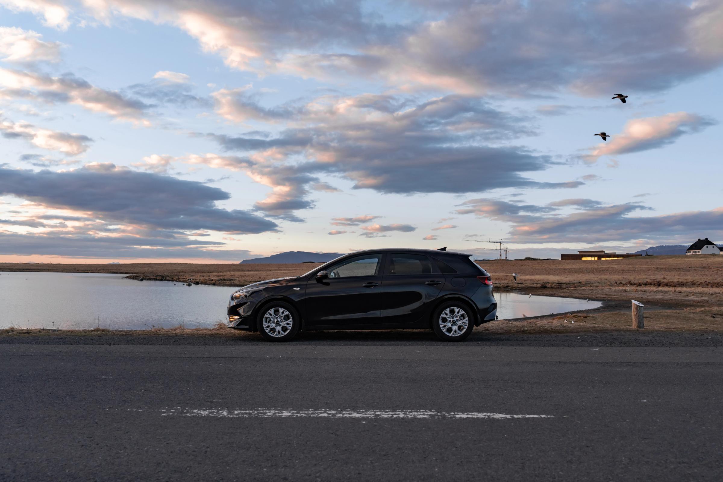 Kia Ceed rental car in Iceland parked beside a lake at sunset