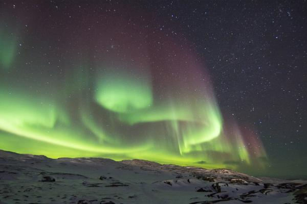 the aurora borealis is dancing in the night sky over a snowy mountain in iceland.
