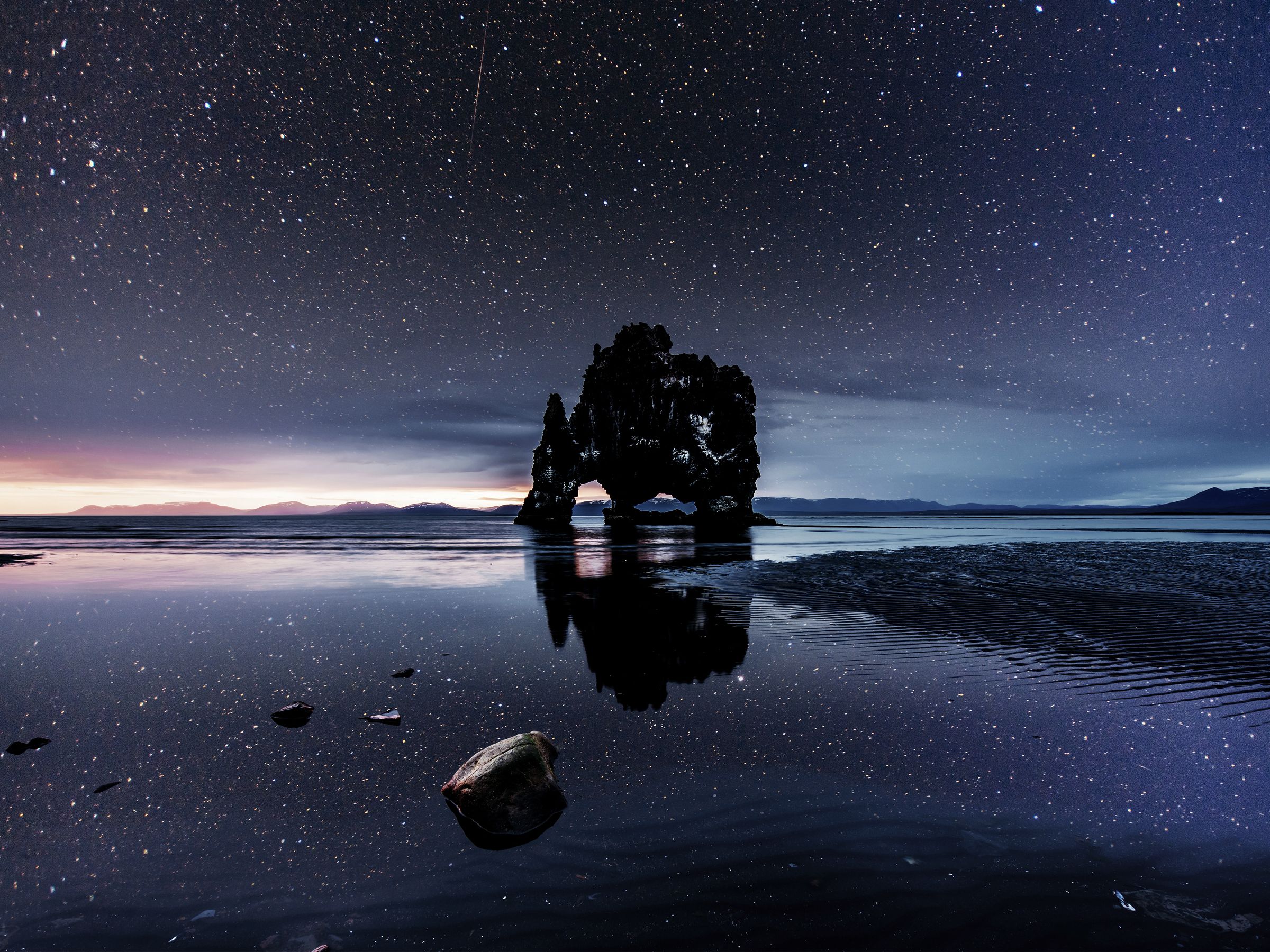 a large rock is sitting in the middle of a body of water under a starry sky .