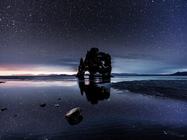 a large rock is sitting in the middle of a body of water under a starry sky .