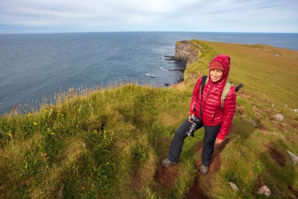 a woman in a red jacket is standing on a cliff overlooking the ocean .