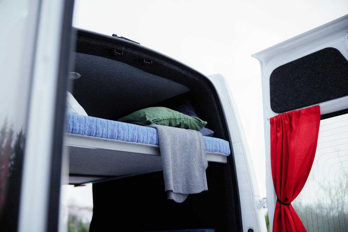 Decke, die vom oberen Bett zwischen den geöffneten Hecktüren eines großen Campers für 5 Personen herunterhängt