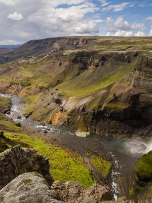 A powerful waterfall plunges into a river winding through a vast green and rocky canyon.