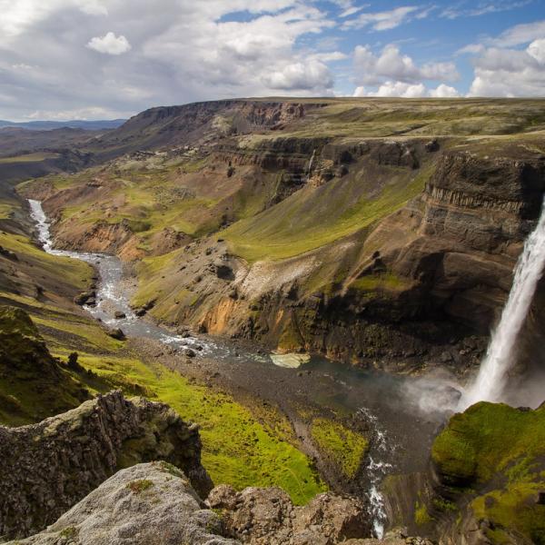 A wide view of a deep canyon with a river, and a tall waterfall plunging into it on the right.