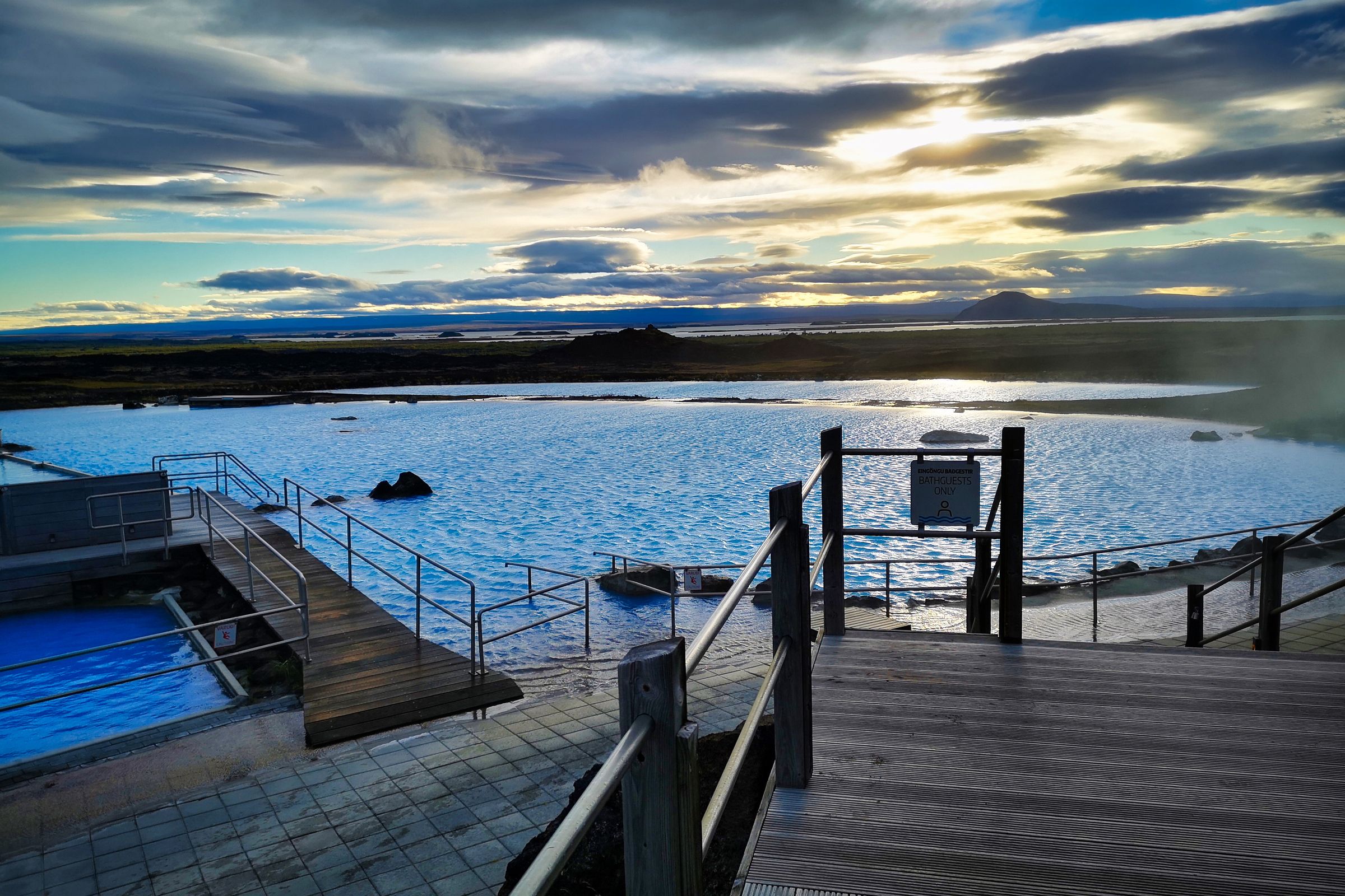 Una laguna geotérmica de un azul intenso, con pasarelas de madera y vapor elevándose bajo un cielo dramático.