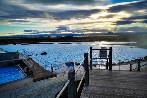A bright blue geothermal lagoon with wooden walkways and steam, under a dramatic sky.