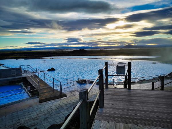 Light blue geothermal pools with wooden walkways under a cloudy sky with sunlight.
