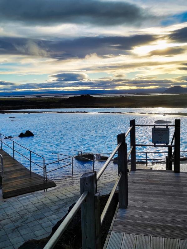 Vibrant blue geothermal hot springs with wooden walkways under a cloudy sky.