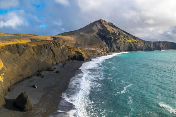an aerial view of a black sandy beach with a Festarfjall mountain in the background