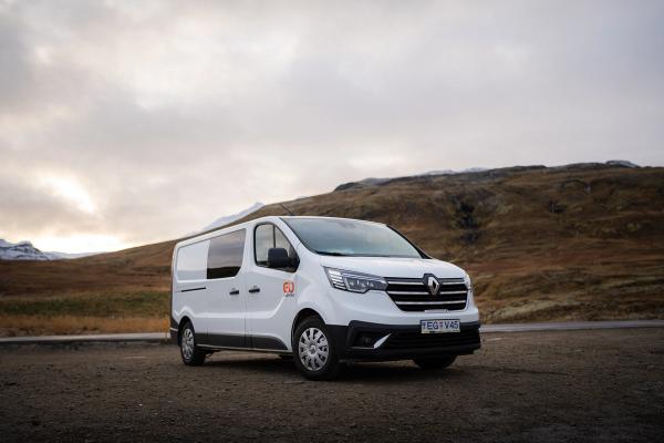 White Renault van with 'GO' logo parked on a dirt road, surrounded by mountains under a cloudy sky.