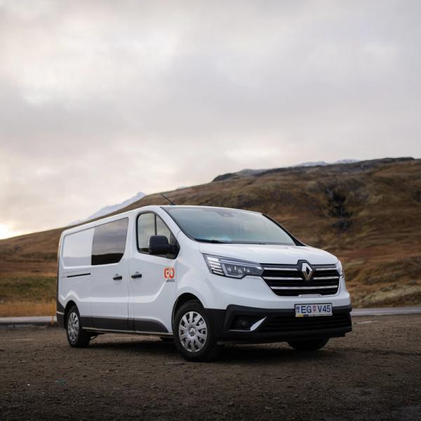 una furgoneta blanca está aparcada al lado de la carretera frente a una montaña.
