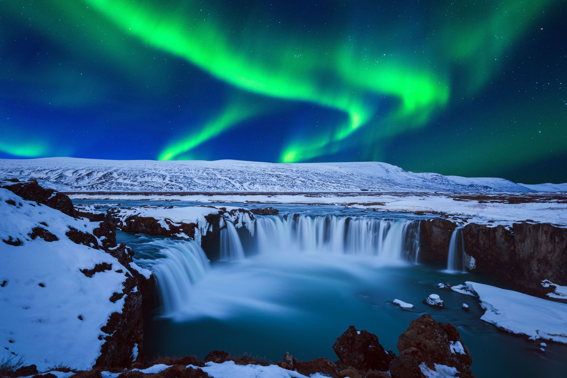 panorámica de una gran cascada por la noche en invierno con la Aurora Boreal en el cielo