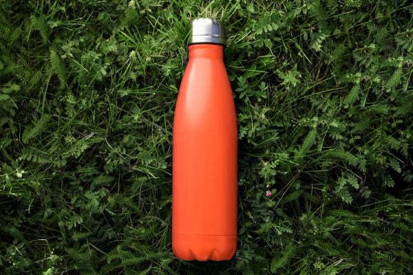 an orange water bottle is sitting on top of a lush green field .