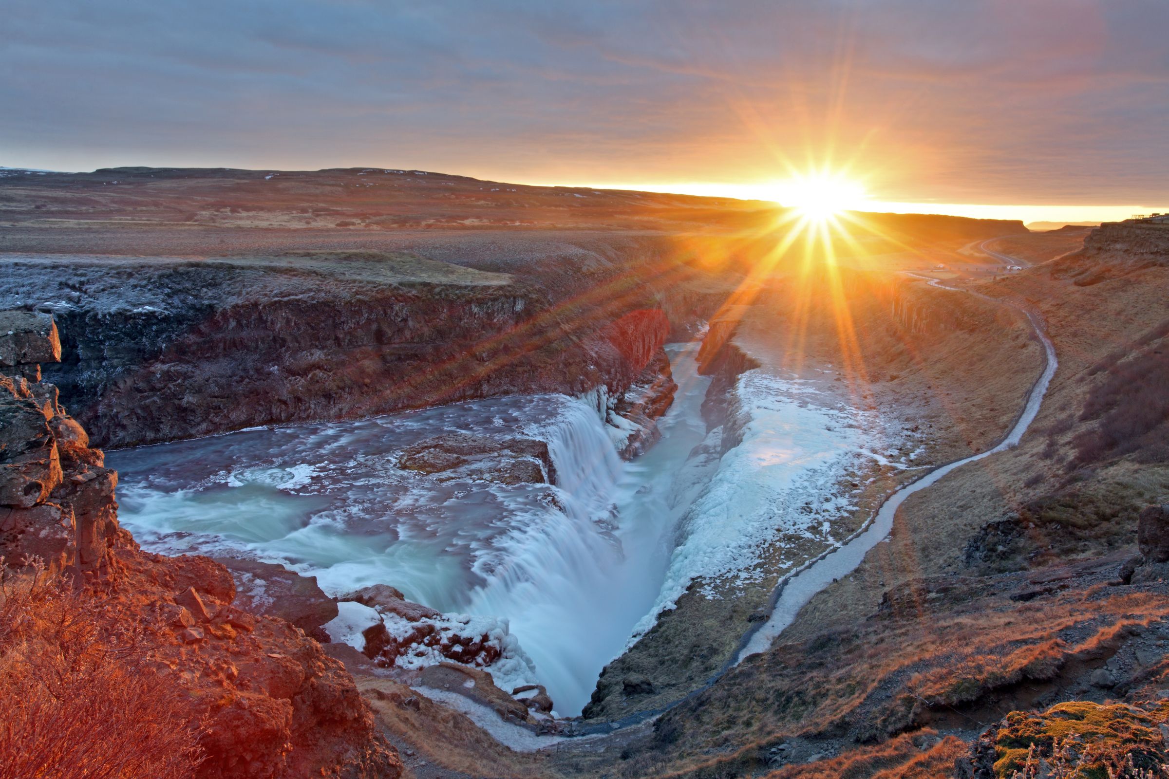the sun is setting over Gullfoss waterfall in the middle of a canyon .
