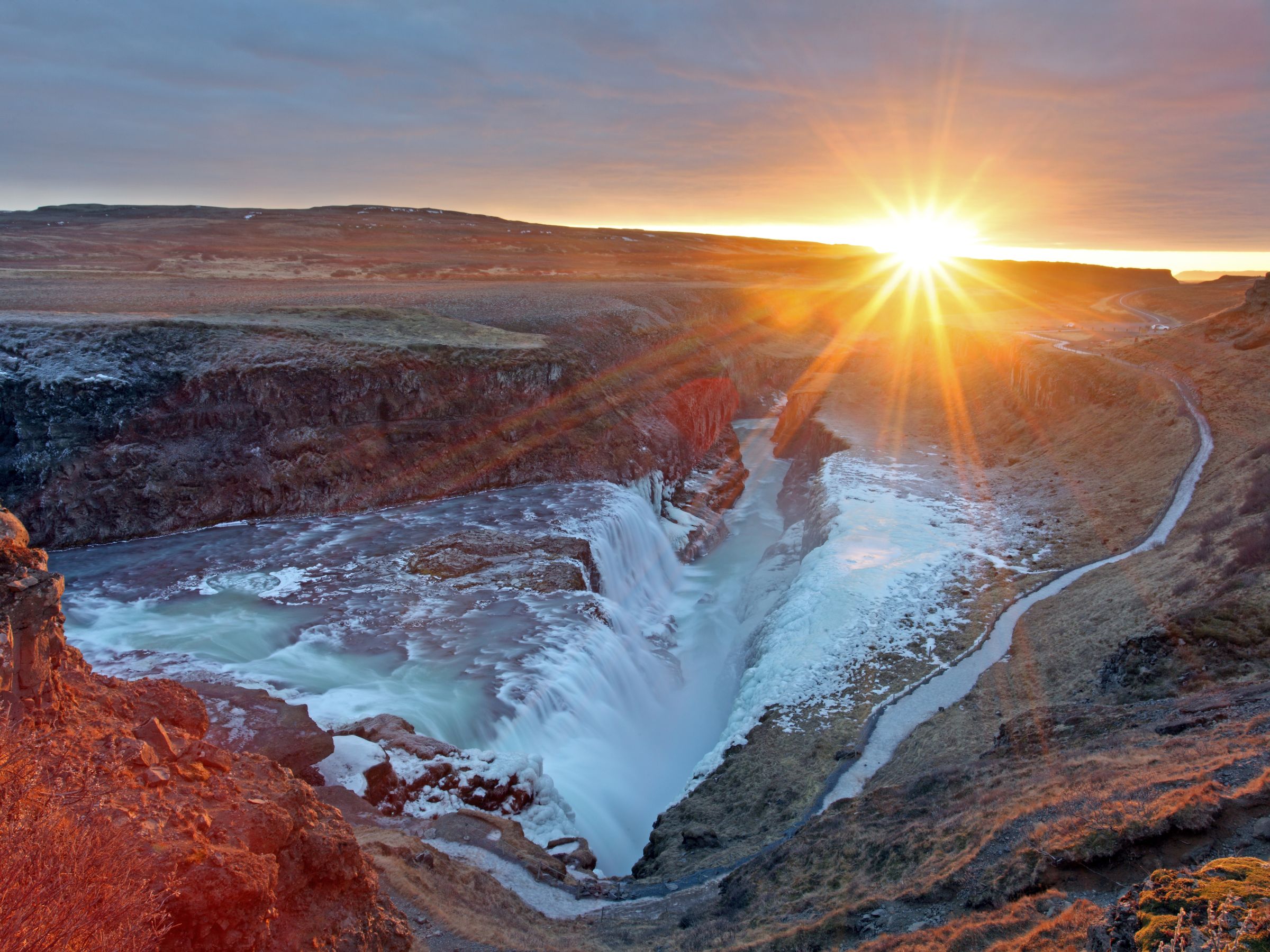 the sun is setting over Gullfoss waterfall in the middle of a canyon .
