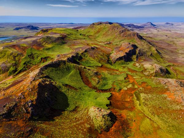 Vibrant green and rust-colored hills under a blue sky with a distant ocean.
