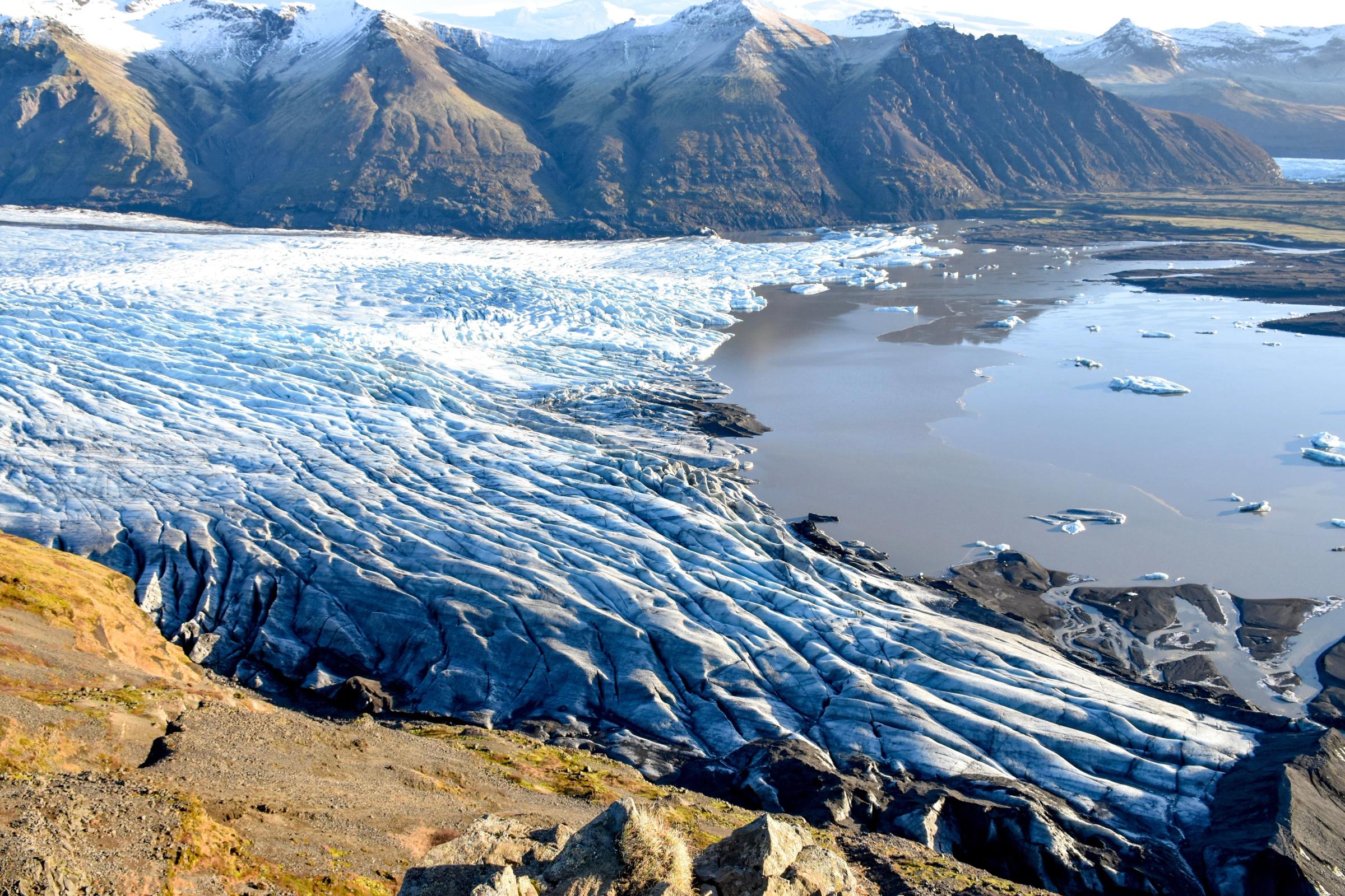 a large glacier in the middle of a lake with mountains in the background .