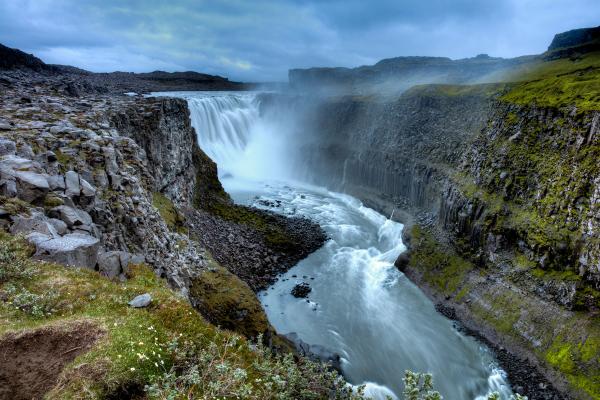 una cascada en medio de un río rodeada de rocas y hierba.