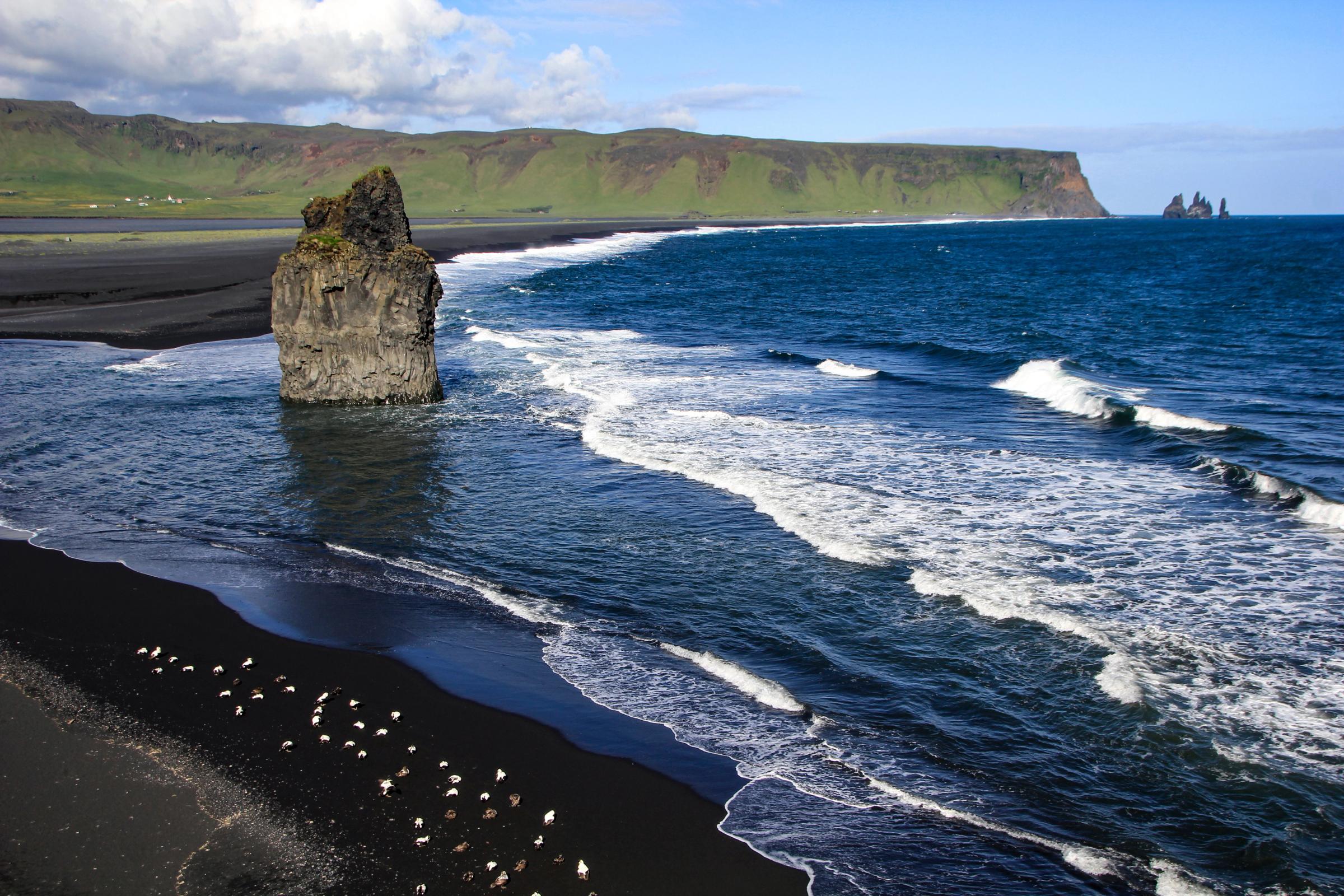 una gran roca en medio del océano junto a una playa de arena negra.