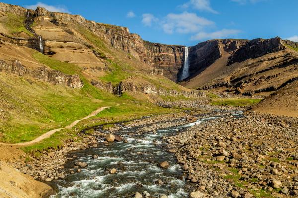 a river flowing through a rocky valley with Hengifoss waterfall in the background .