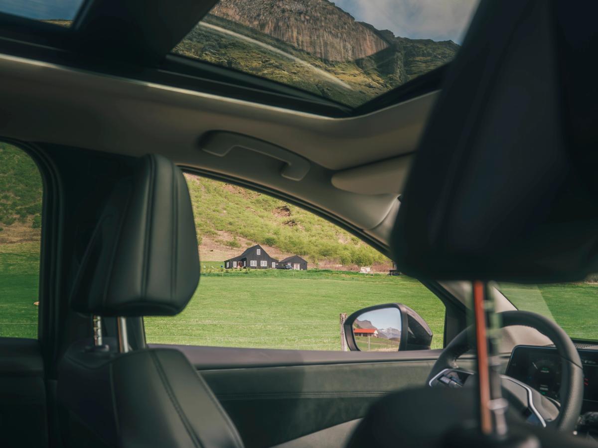 Nissan Ariya með víðáttumiklu glerþaki Innrétting Nissan Ariya með víðáttumiklu glerþaki og útsýni yfir fjöll og sveitabyggingar