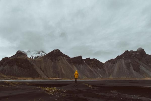 a man in a yellow raincoat is standing in front of a mountain range .
