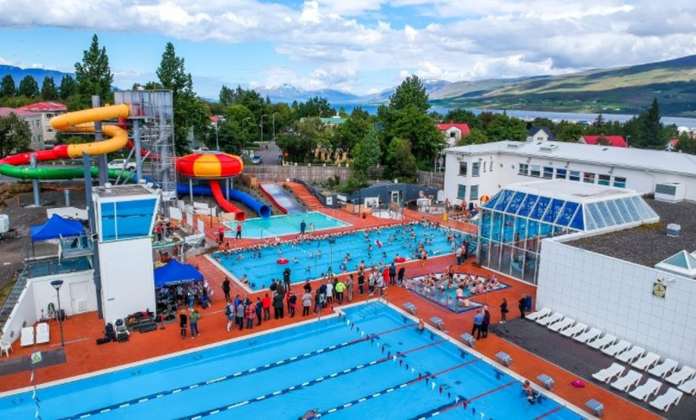 an aerial view of a swimming pool with a water slide in the background in akureyri in iceland.