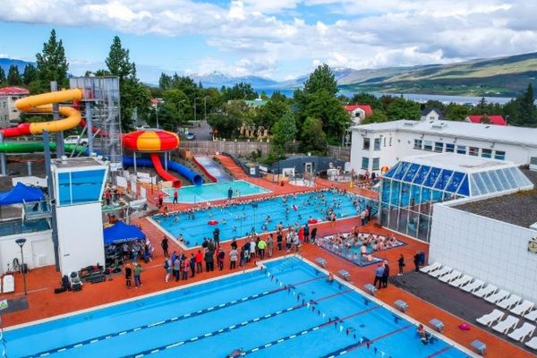 an aerial view of a swimming pool with a water slide in the background in akureyri in iceland.