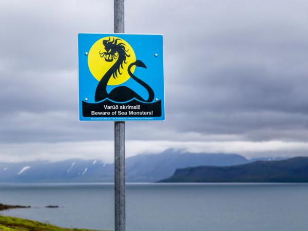 a sign on a pole warning people to beware of sea monsters .