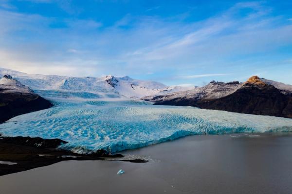 an aerial view of a large glacier in the middle of a lake surrounded by snow covered mountains .