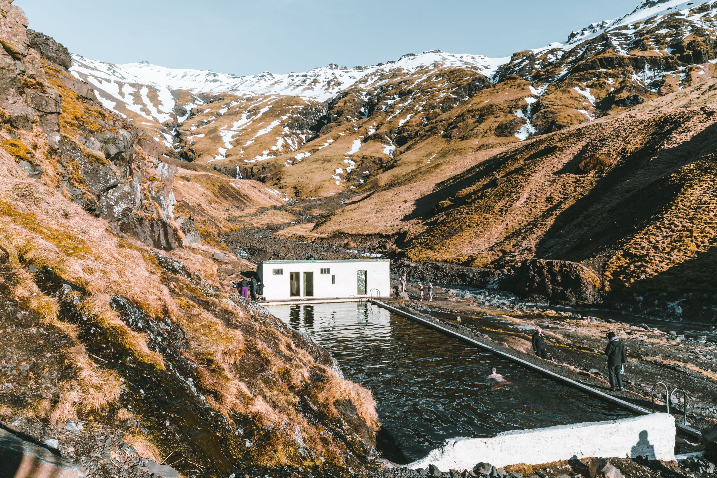 a man is standing next to Seljavallalaug pool, in the middle of a mountain .