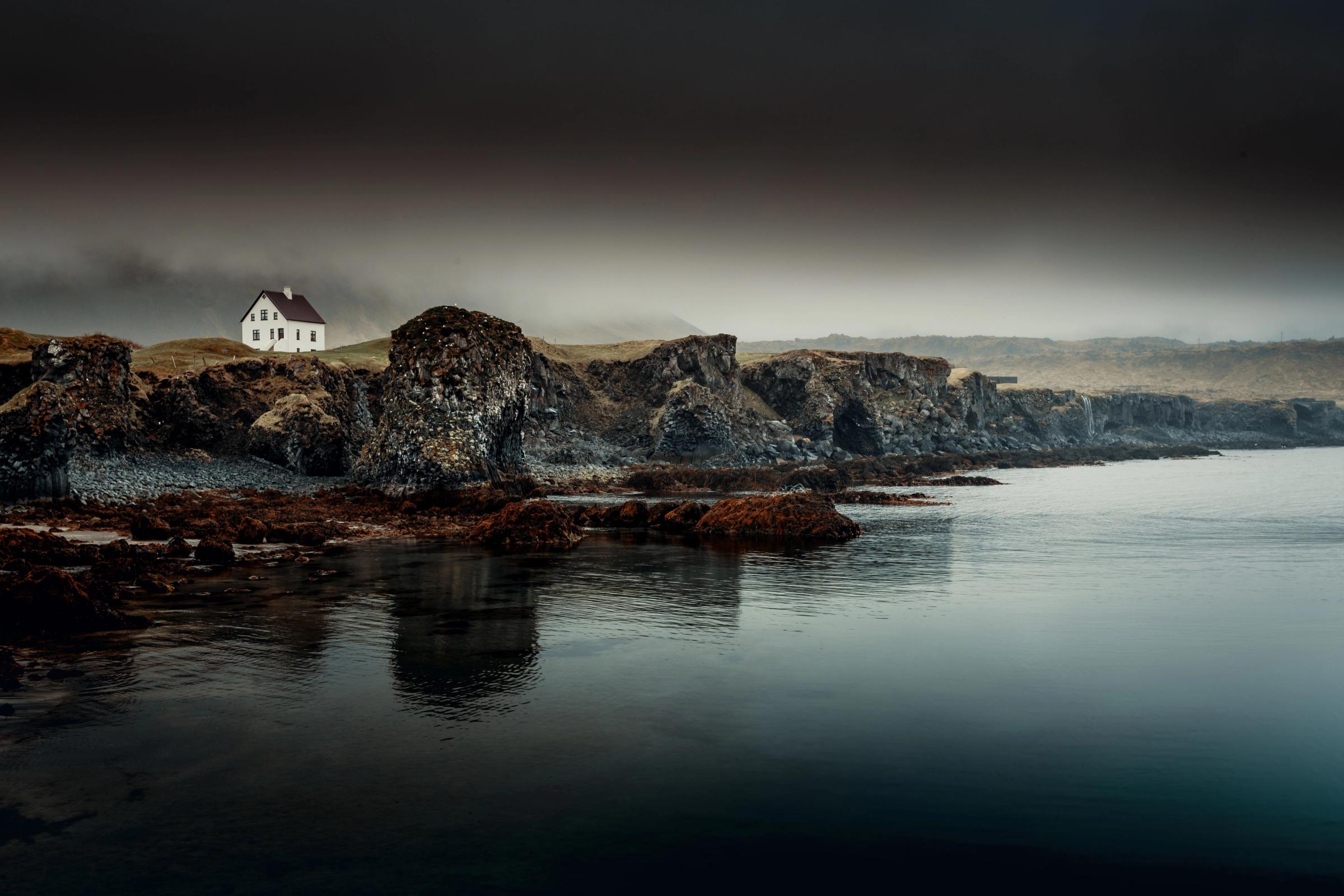a small white house is sitting on top of a rocky cliff next to a body of water .